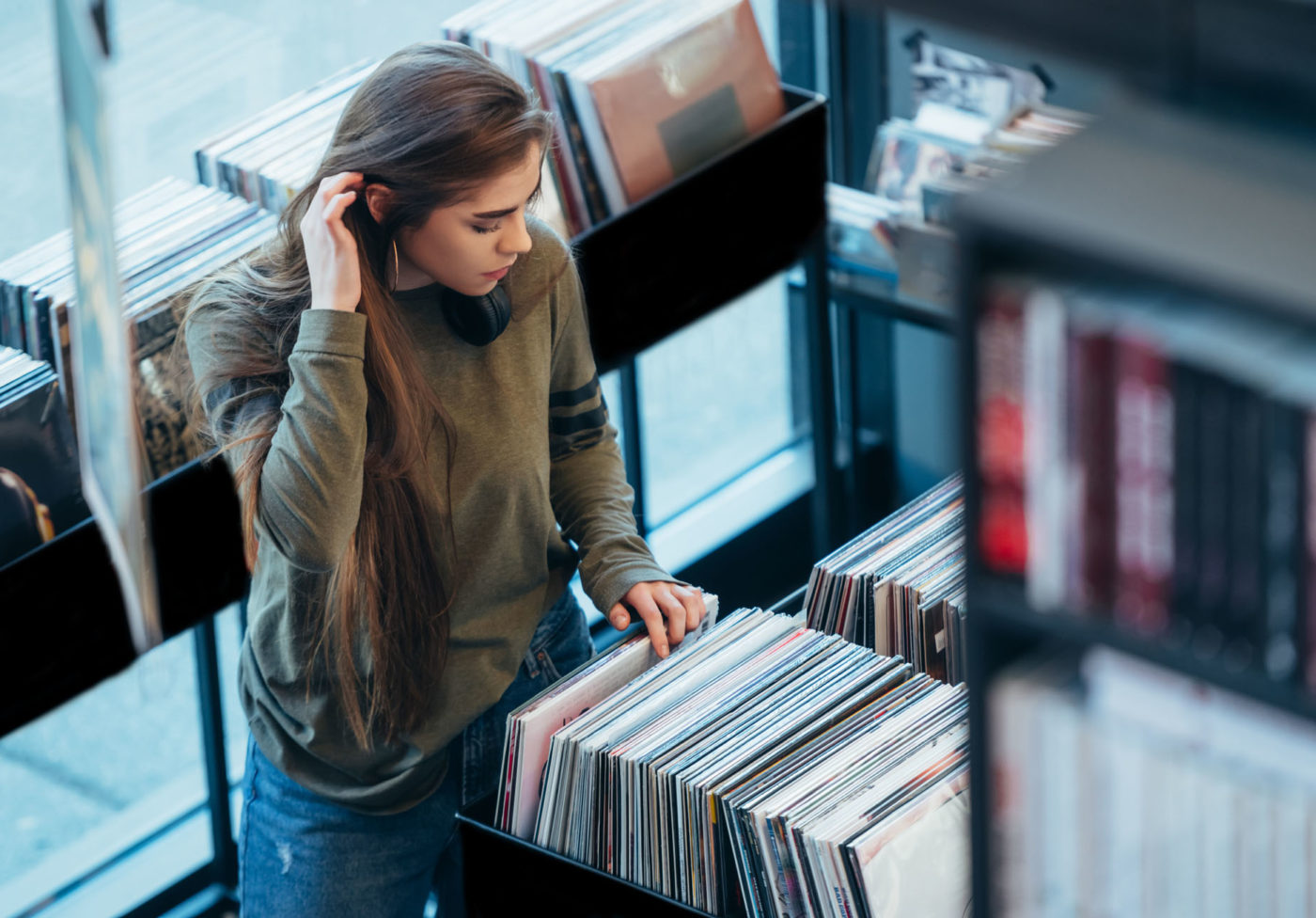 Gorgeous young woman looking for vinyl records in a vintage store. Vintage and retro style.